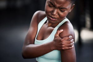 a young woman holding her shoulder in pain while at the gym